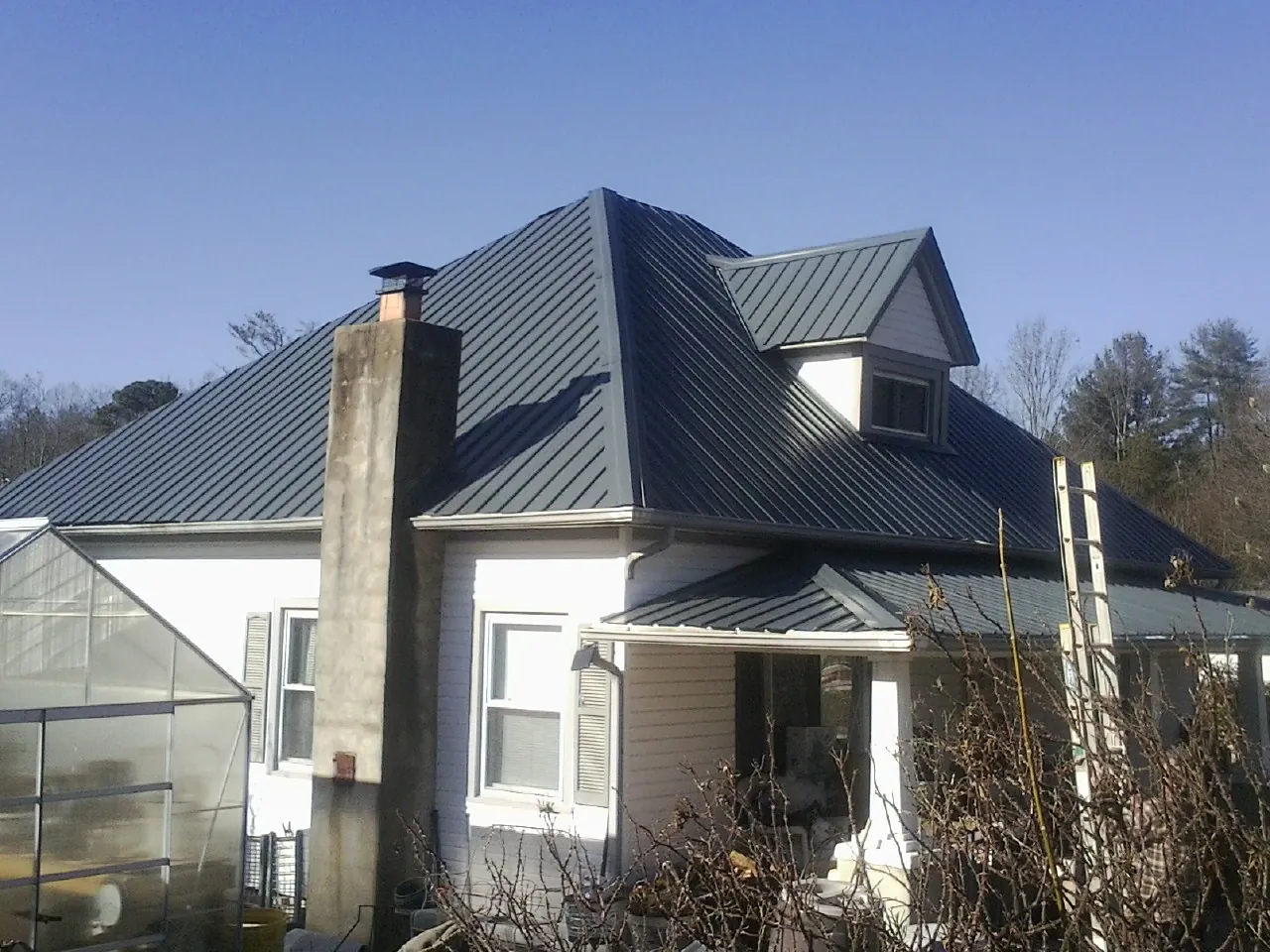 Dark blue standing seam metal roof on a white farmhouse with dormer — Slate & Tile Roof Repair by Roofing Brothers in Ovando