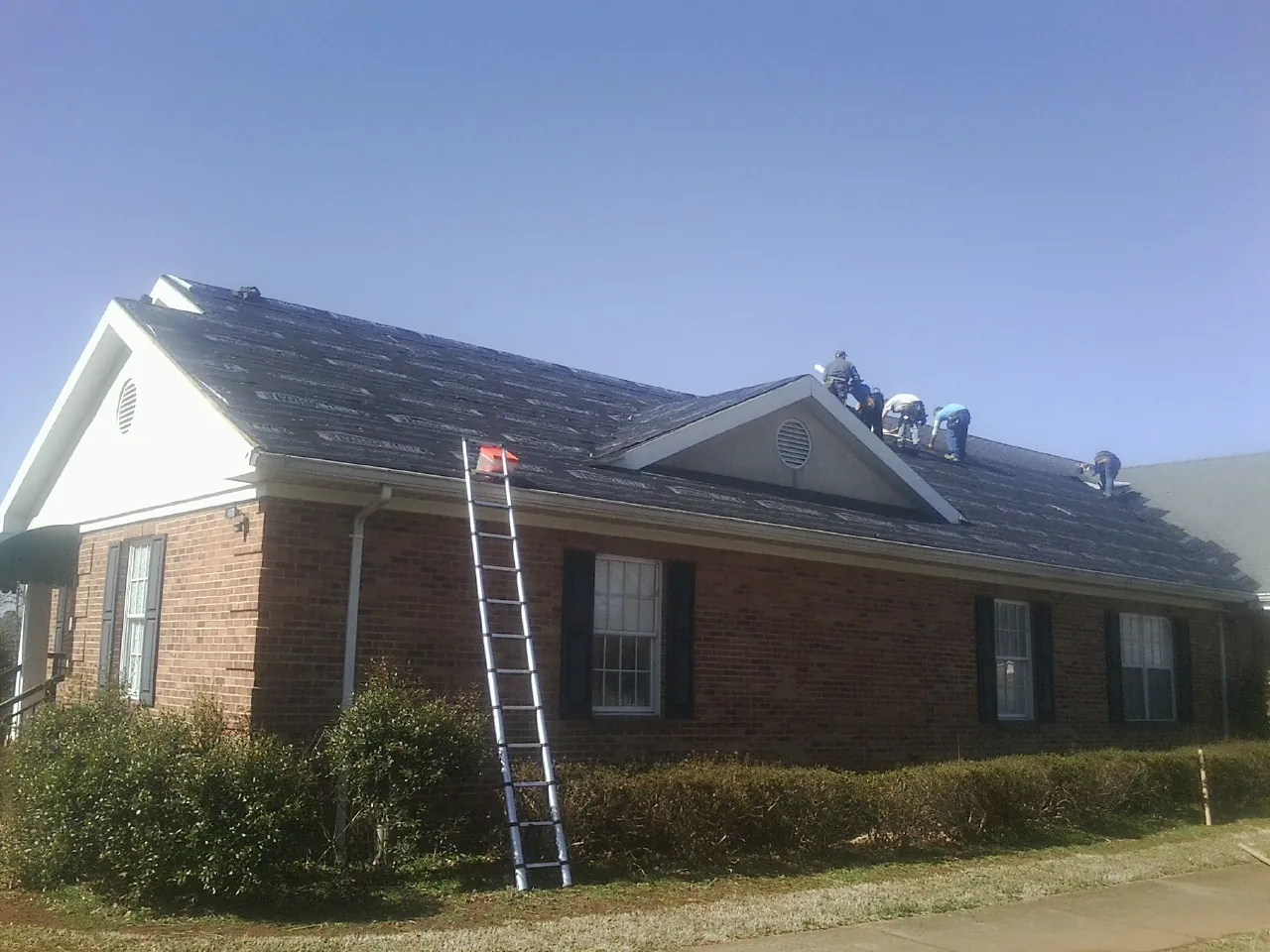 Crew tearing shingles off a brick ranch roof with a ladder set — Emergency Roof Repair work by our crew in Ovando