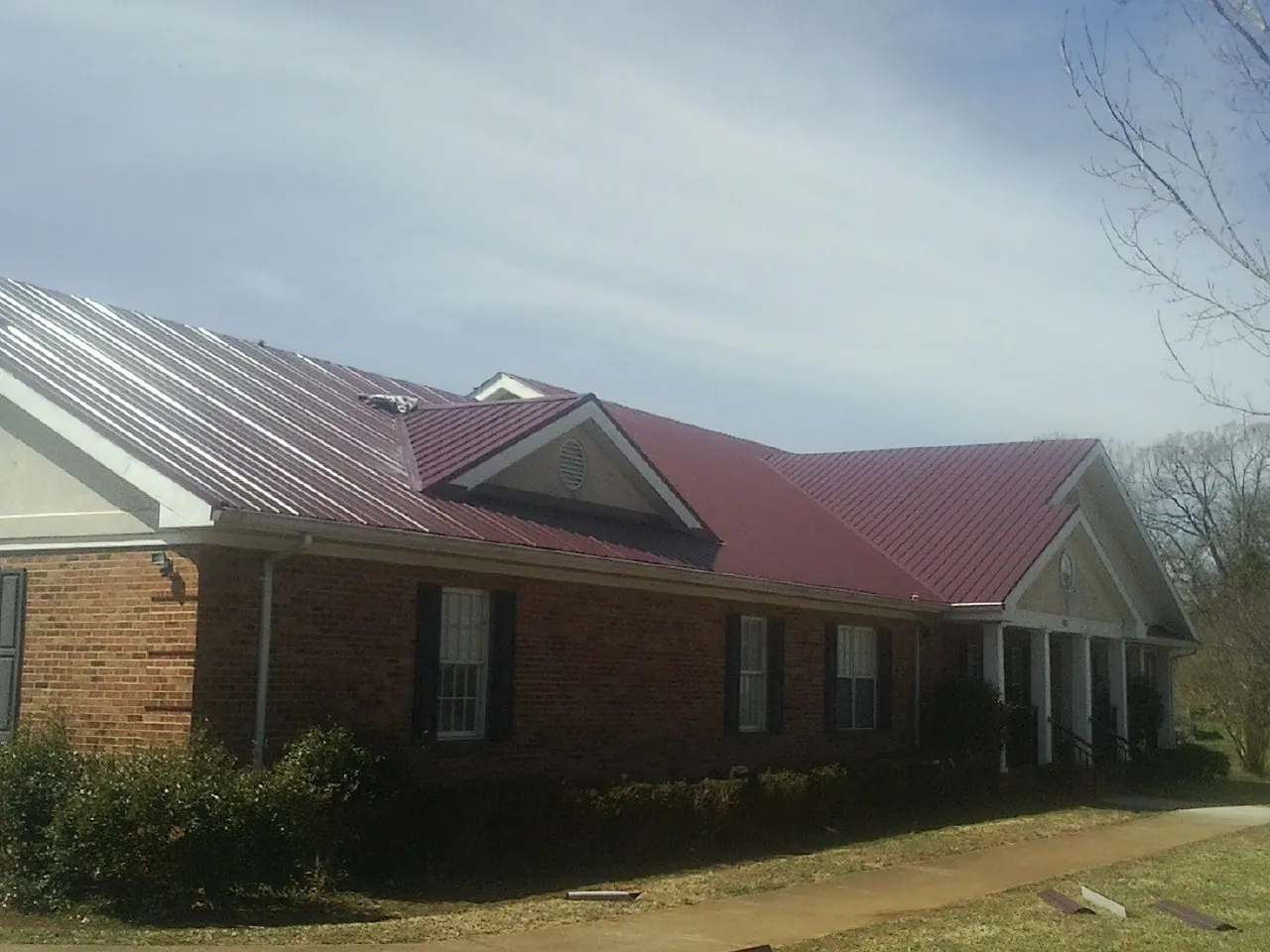 Red metal roof with gabled entries on a long brick building, from a Hail Damage Roof Repair job in Ovando