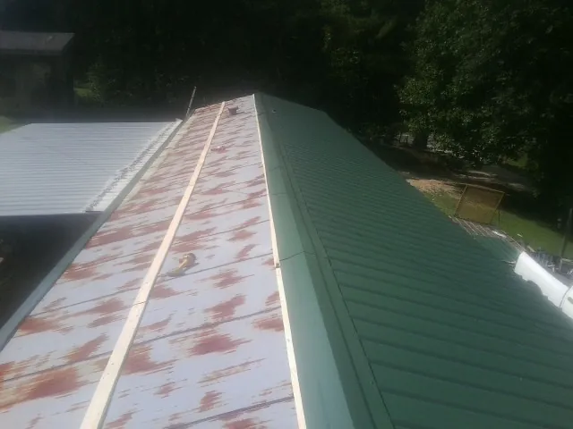 Old rusted panels beside newly installed green metal roofing — Wind Damage Roof Repair by Roofing Brothers in Ovando