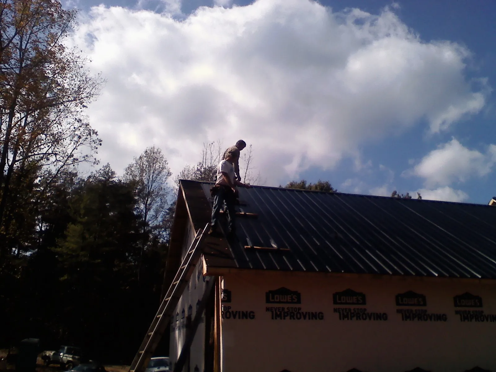 Roofer fastening dark metal panels high against a cloudy sky, from a Roof Inspection job in Ovando