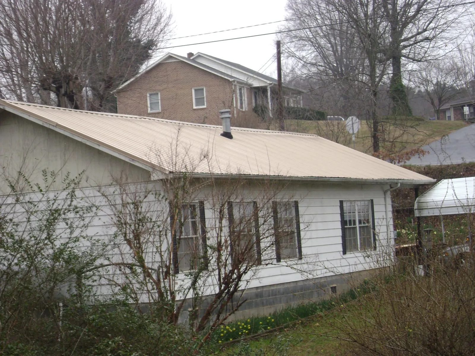 Tan metal roof on a white sided house set into a hillside — Commercial Roofing by Roofing Brothers in Ovando